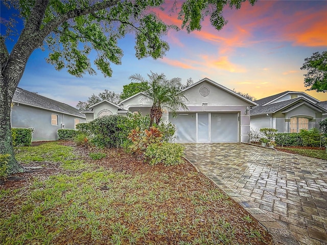 ranch-style home featuring a garage, decorative driveway, and stucco siding