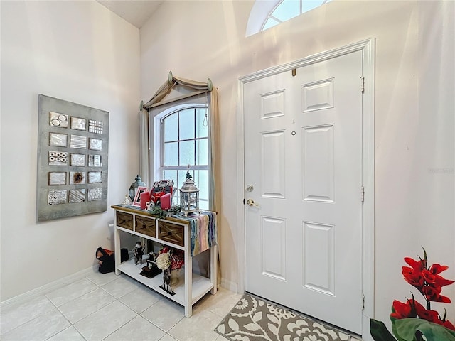 interior space with light tile patterned flooring, a towering ceiling, and baseboards