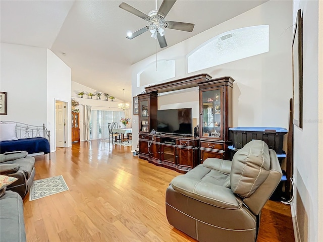 living area with high vaulted ceiling, ceiling fan with notable chandelier, visible vents, and wood finished floors