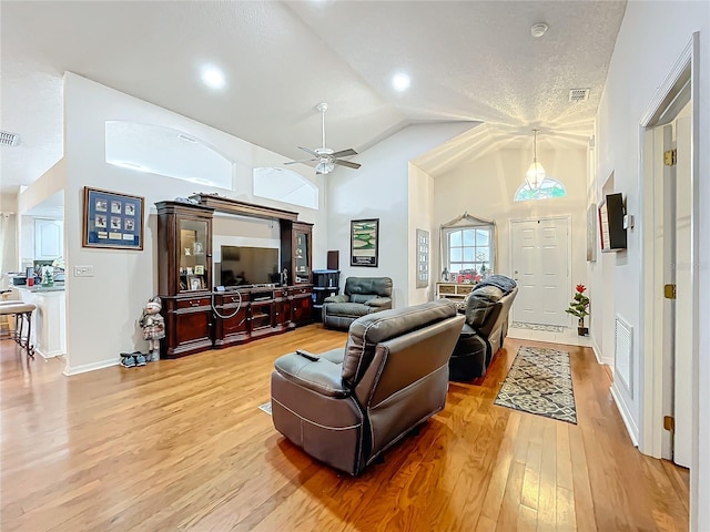 living room with a ceiling fan, visible vents, high vaulted ceiling, and wood finished floors