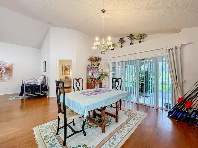 dining space featuring wood finished floors, vaulted ceiling, a textured ceiling, and an inviting chandelier