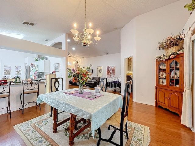 dining room featuring a textured ceiling, high vaulted ceiling, wood finished floors, visible vents, and an inviting chandelier