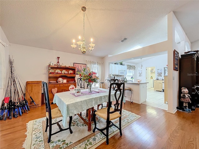 dining room featuring lofted ceiling, a textured ceiling, light wood-style flooring, a notable chandelier, and visible vents