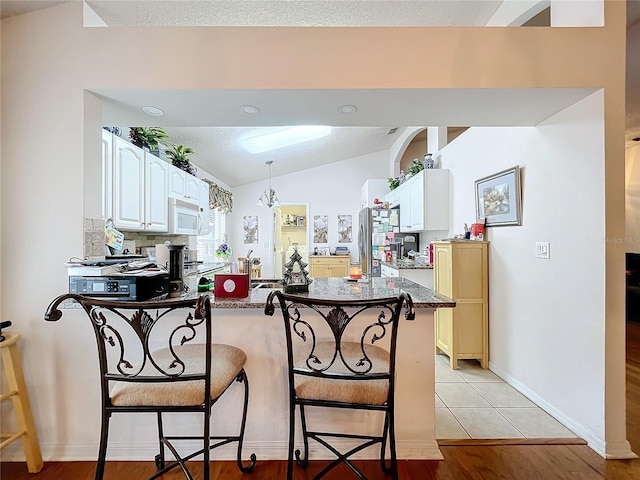 kitchen with lofted ceiling, white microwave, a breakfast bar area, a peninsula, and white cabinets