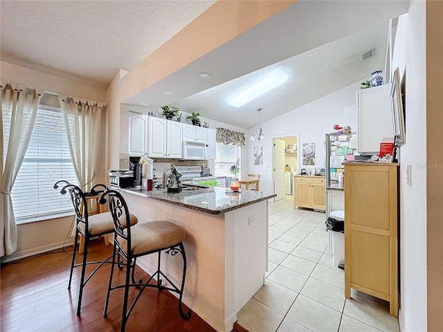 kitchen with white appliances, dark stone counters, white cabinets, decorative light fixtures, and a peninsula