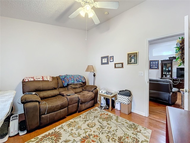 living area with ceiling fan, a textured ceiling, baseboards, and wood finished floors