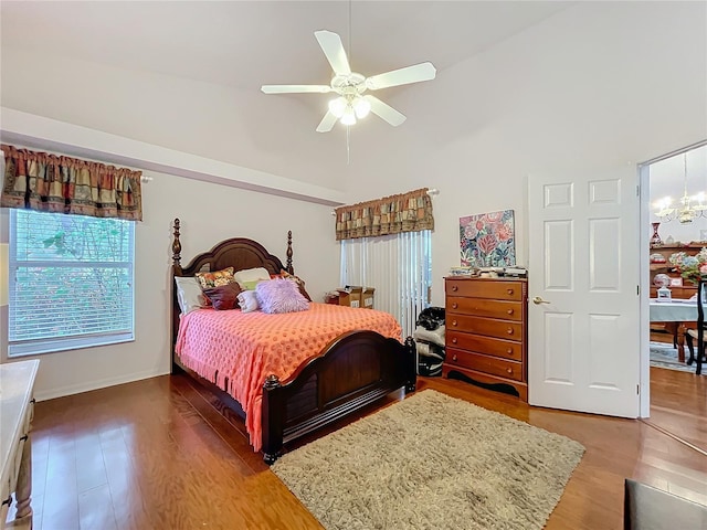 bedroom featuring high vaulted ceiling, wood finished floors, and ceiling fan with notable chandelier