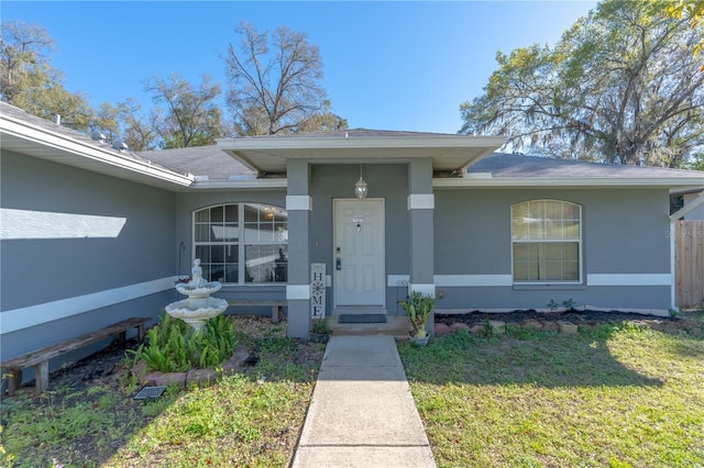 doorway to property with stucco siding, a lawn, and a shingled roof