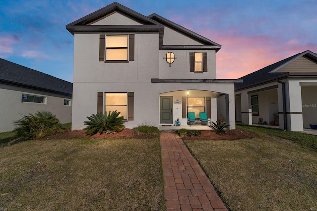 back of property at dusk featuring a lawn and stucco siding