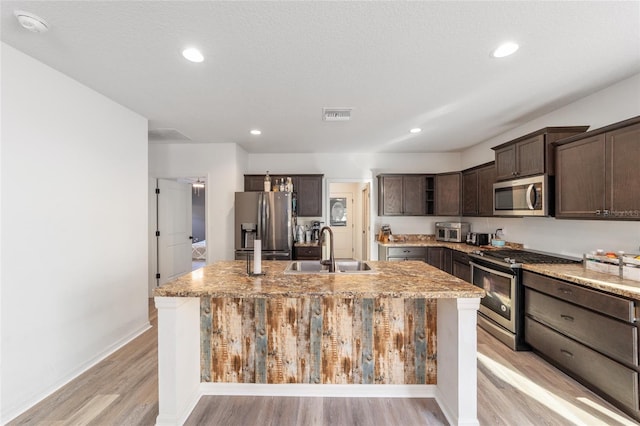 kitchen featuring an island with sink, light stone counters, stainless steel appliances, and a sink