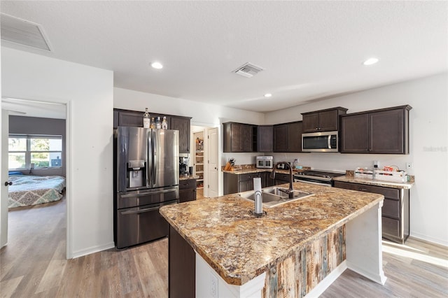 kitchen with a kitchen island with sink, dark brown cabinetry, a sink, visible vents, and appliances with stainless steel finishes