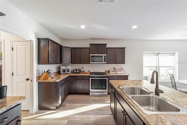 kitchen with recessed lighting, stainless steel appliances, a sink, light wood-style floors, and dark brown cabinets