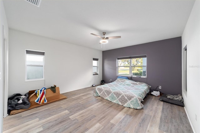 bedroom with light wood finished floors, a ceiling fan, visible vents, and baseboards