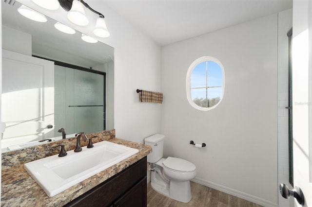 bathroom featuring toilet, a shower with shower door, wood finished floors, vanity, and baseboards