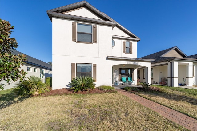 rear view of property with covered porch, a lawn, and stucco siding