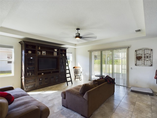 living area featuring ceiling fan, a textured ceiling, visible vents, tile patterned floors, and a raised ceiling