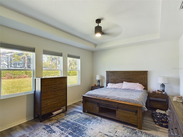 bedroom featuring a raised ceiling, dark wood finished floors, and baseboards