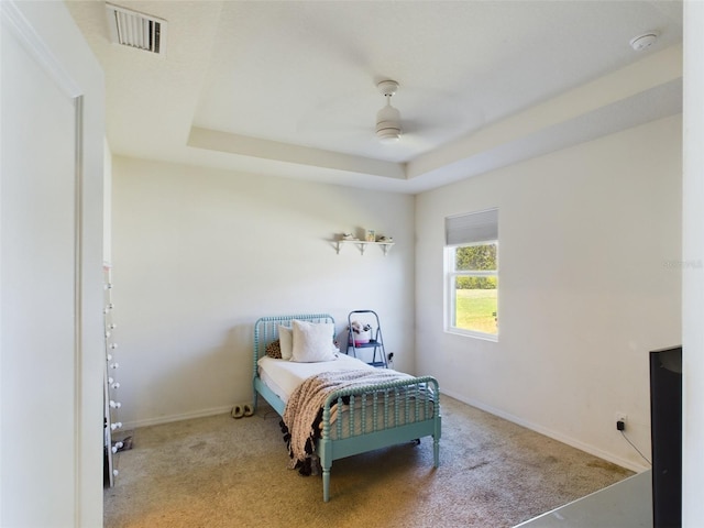 bedroom featuring a ceiling fan, visible vents, baseboards, a tray ceiling, and carpet