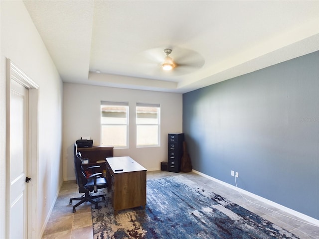 office featuring a raised ceiling, ceiling fan, and baseboards