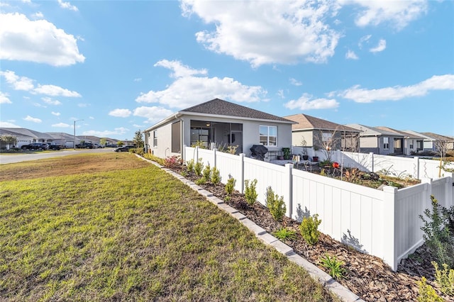 view of property exterior featuring a sunroom, a fenced backyard, a residential view, a yard, and stucco siding