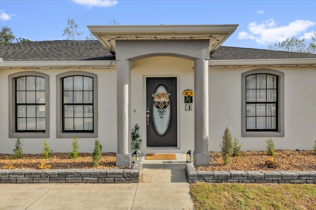 view of exterior entry with roof with shingles and stucco siding