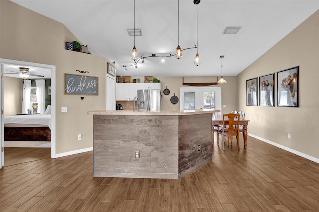 kitchen with lofted ceiling, stainless steel fridge, visible vents, and wood finished floors