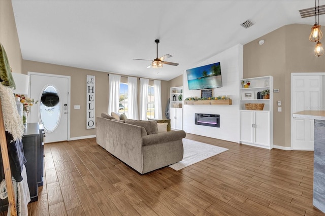 living area with lofted ceiling, visible vents, a glass covered fireplace, ceiling fan, and wood finished floors