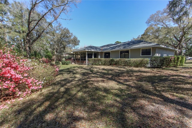 back of house featuring a sunroom, a lawn, and stucco siding