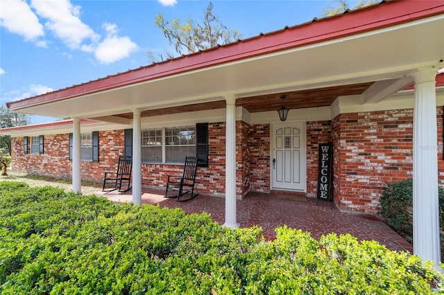 entrance to property featuring covered porch and brick siding