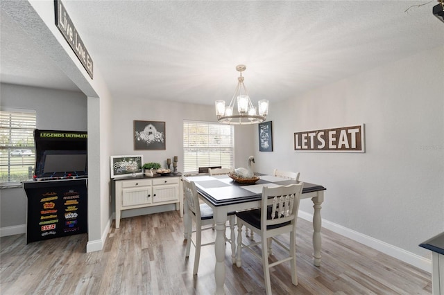 dining space featuring baseboards, a textured ceiling, an inviting chandelier, and light wood-style floors