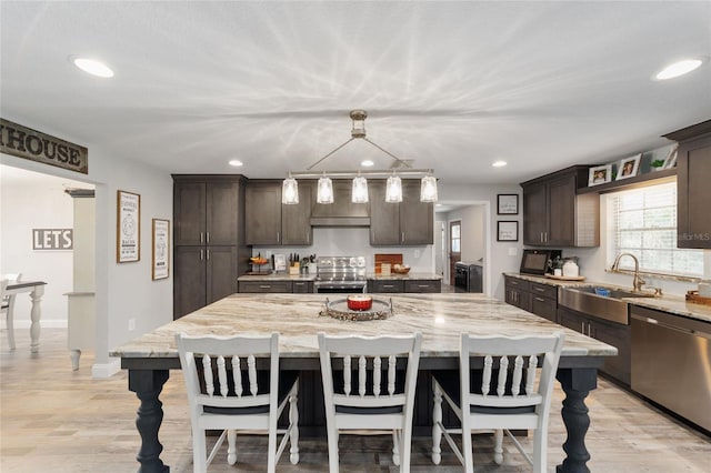 kitchen featuring dark brown cabinetry, a breakfast bar, a sink, appliances with stainless steel finishes, and light stone countertops