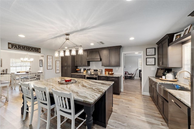 kitchen with dark brown cabinetry, visible vents, stainless steel appliances, premium range hood, and a sink