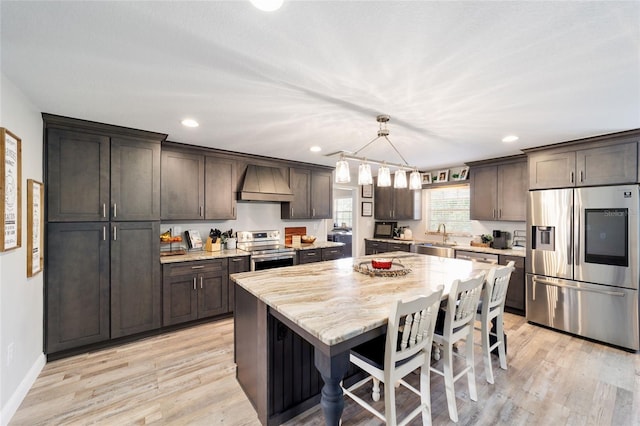 kitchen with custom exhaust hood, stainless steel appliances, a sink, dark brown cabinets, and light wood-type flooring