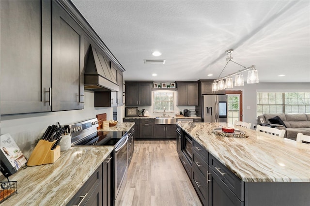 kitchen with light stone counters, appliances with stainless steel finishes, a sink, light wood-type flooring, and premium range hood