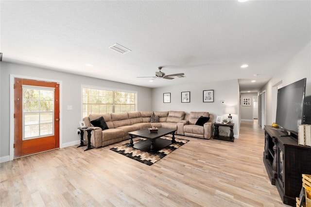 living room featuring baseboards, visible vents, ceiling fan, a textured ceiling, and light wood-type flooring