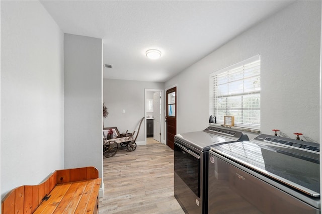 clothes washing area featuring washing machine and dryer, laundry area, visible vents, and light wood finished floors