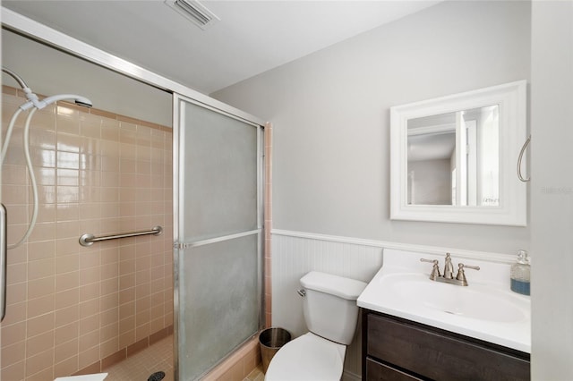 bathroom with visible vents, wainscoting, toilet, vanity, and a shower stall