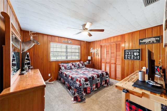 bedroom with light carpet, visible vents, ceiling fan, wood walls, and a closet