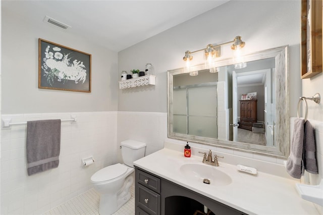 bathroom with visible vents, toilet, a wainscoted wall, an enclosed shower, and tile walls