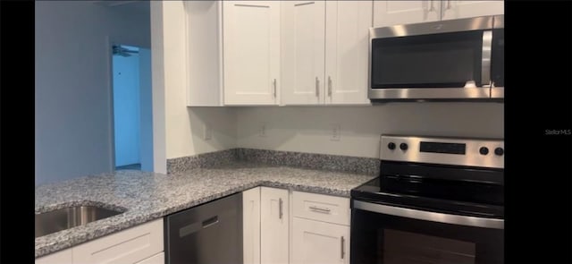 kitchen with stainless steel appliances, light stone counters, a sink, and white cabinetry