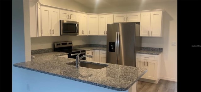 kitchen with appliances with stainless steel finishes, white cabinetry, a sink, dark stone countertops, and a peninsula