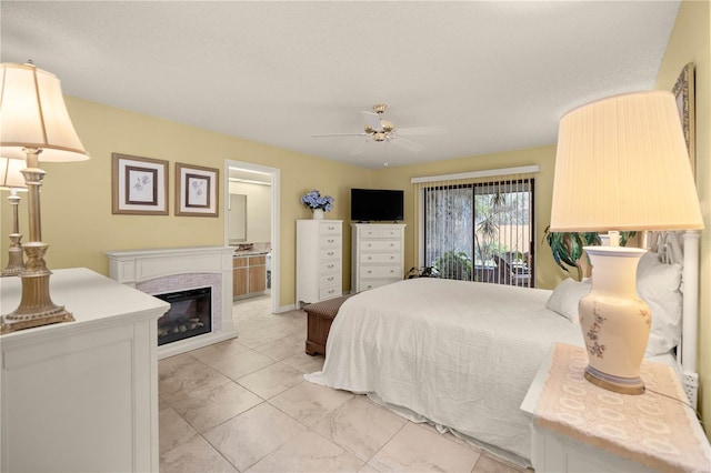 bedroom featuring connected bathroom, a ceiling fan, and a glass covered fireplace