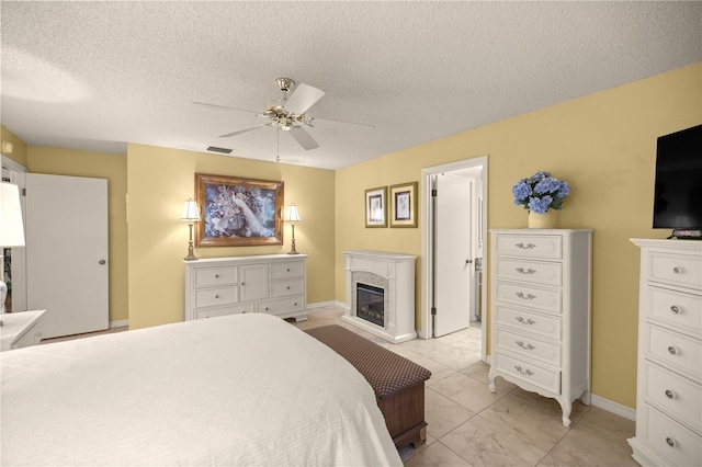 bedroom featuring visible vents, a ceiling fan, a glass covered fireplace, a textured ceiling, and baseboards