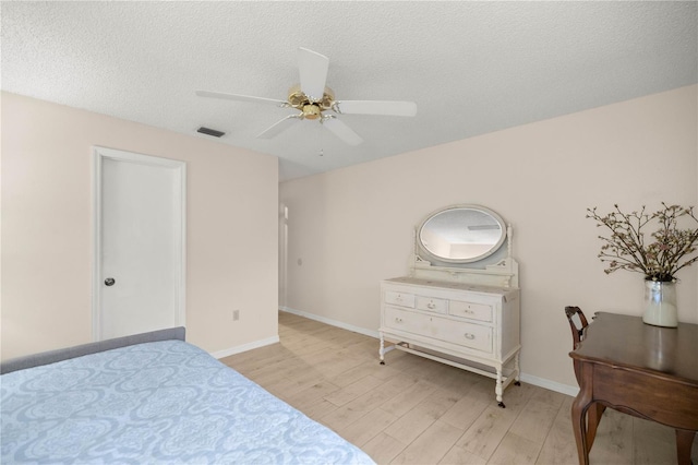 bedroom featuring a textured ceiling, ceiling fan, visible vents, baseboards, and light wood finished floors