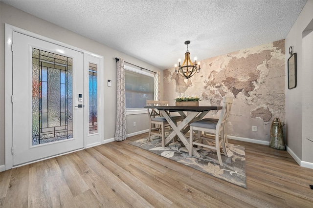 unfurnished dining area featuring an inviting chandelier, a textured ceiling, baseboards, and wood finished floors