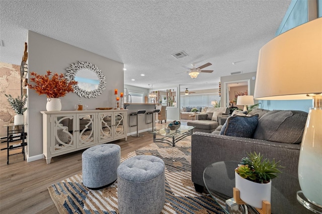 living room featuring a ceiling fan, visible vents, a textured ceiling, and wood finished floors