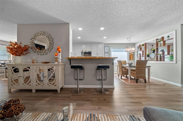 bar featuring baseboards, stainless steel microwave, wood finished floors, and a notable chandelier