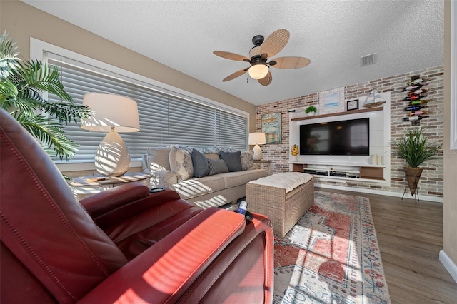 living area with brick wall, a textured ceiling, visible vents, and wood finished floors