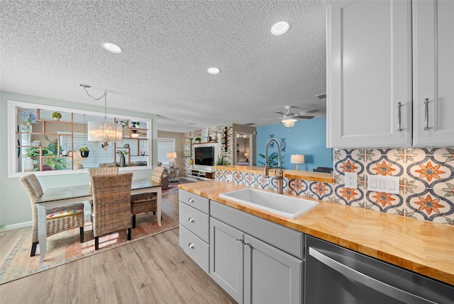 kitchen featuring stainless steel dishwasher, light wood-style floors, wooden counters, a sink, and ceiling fan with notable chandelier