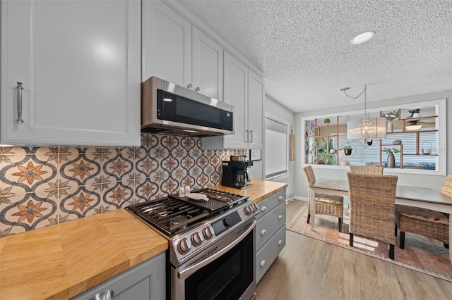 kitchen featuring light wood finished floors, butcher block countertops, stainless steel appliances, a chandelier, and backsplash